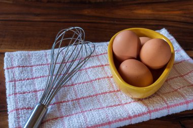 Sarı kasede çiğ tavuk yumurtası ve ahşap arka planda çırpılmış çırpma. Pişirme konseptine başlamaya hazır