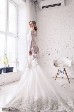 Gelin, sabahlığı ve iç çamaşırı giymiş pencere duruyor ve gelinlik onun elinde tutar. Sabah gelinin