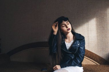 Deri ceketli güzel kız kanepede bir odada oturur.