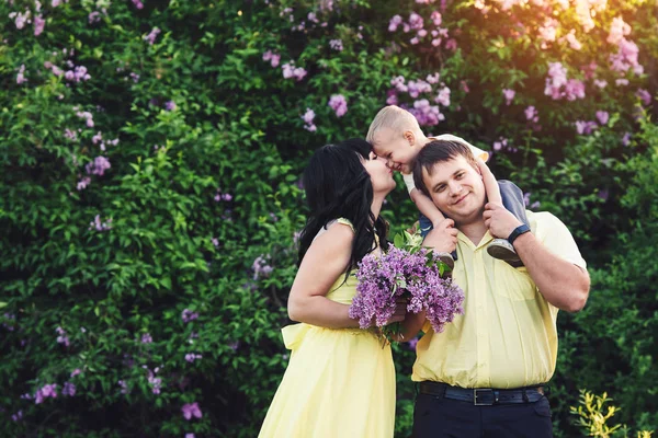 Gelukkige familie in park met bloeiende lila. Moeder, vader en zoon gelukkig lopen bij zonsondergang. Concept van gelukkige familie. — Stockfoto