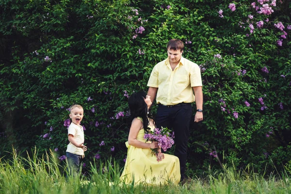 Щаслива родина в парку з квітучим бузком. Мама, тато і син щасливі ходити на заході сонця. Концепція щасливої сім'ї. Син широко посміхається . — стокове фото