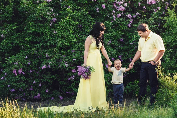 Familia feliz en el parque con la floración lila. Mamá, papá y bebé caminan felices al atardecer. Concepto de familia feliz — Foto de Stock