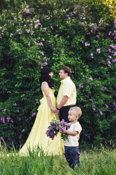 ライラックの咲くを公園で幸せな家族。お母さん、お父さんと息子の幸せは、夕日で歩きます。幸せな家族の概念. — ストック写真