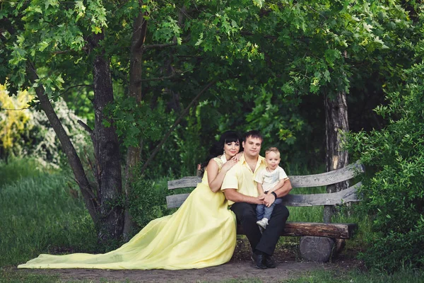 Familia en ropa amarilla está sentado en el parque en el banco en verano, y el hijo muestra la lengua — Foto de Stock