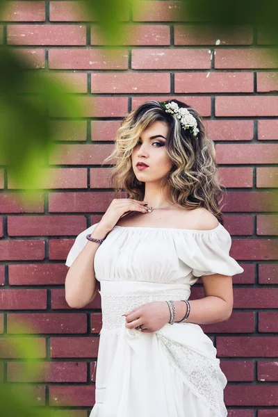 Menina bonita em vestido branco está de pé perto da parede de tijolo e posando — Fotografia de Stock