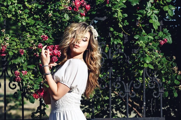Retrato al aire libre de joven hermosa chica rizada cerca de red forjada con rosas . — Foto de Stock