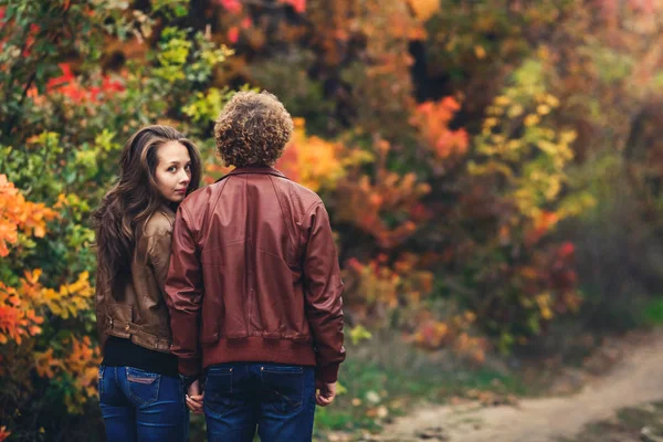 Der lockige Mann drehte ihm den Rücken zu, und hinter seiner Schulter lugt ein Mädchen hervor. Liebendes Paar vor dem Hintergrund schöner bunter Herbstbäume. — Stockfoto