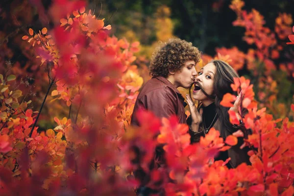 La coppia allegra è cattiva e mostra emozioni tra alberi rossi di autunno. capelli ricci baffuti uomo baci, e la ragazza fa baffi dai suoi capelli . — Foto Stock