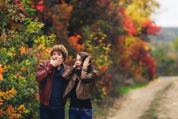 Pareja alegre muestra emociones. hombre y mujer en chaquetas de cuero y jeans muestran sorpresa contra el fondo de los árboles de otoño . —  Fotos de Stock