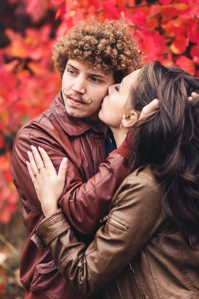 Hombre bigote de pelo rizado y mujer morena abrazándose en otoño contra el fondo de los árboles rojos . —  Fotos de Stock