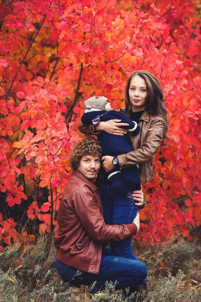 Молода щаслива сім'я, вкрита ковдрою, стоїть біля красивих червоних осінніх дерев . — стокове фото