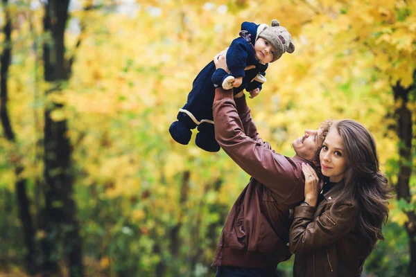 Young happy family in autumn in park. Father joyfully throws his son up. — Stock Photo, Image