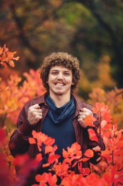 kıvırcık saçlı bıyıklı zararlı adam geniş gülümsüyor ve Ağızlıklar (incir) kırmızı çalılar arasında gösterir.