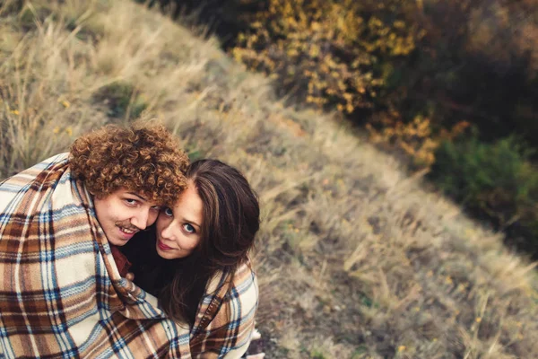 Amando casal bonito sentado na grama e se escondendo atrás do tapete no outono . — Fotografia de Stock