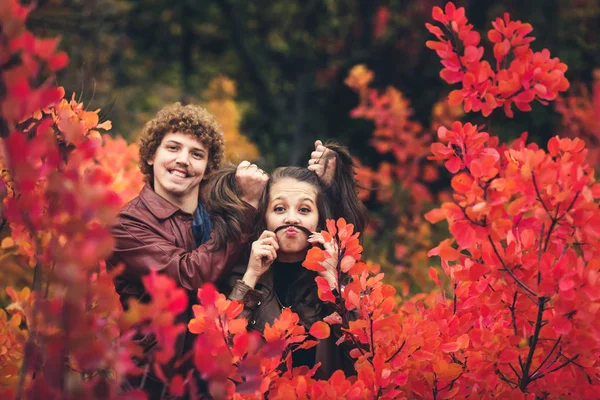 Casal alegre é impertinente e mostra emoções entre árvores vermelhas de outono — Fotografia de Stock