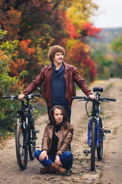 Chico bigote de pelo rizado y una chica de pelo mineral en el stand de otoño con bicicletas en la carretera y mostrar emociones alegres . —  Fotos de Stock