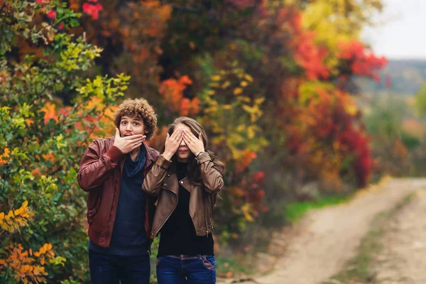 Veselý pár ukazuje emoce. muž a žena v kožených bund a džíny Ukázat překvapení podzimní stromy v pozadí. — Stock fotografie