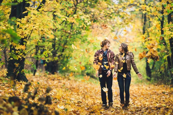 Pareja amorosa en un parque de otoño. Hombre y mujer alegremente arrojan hojas amarillas . —  Fotos de Stock