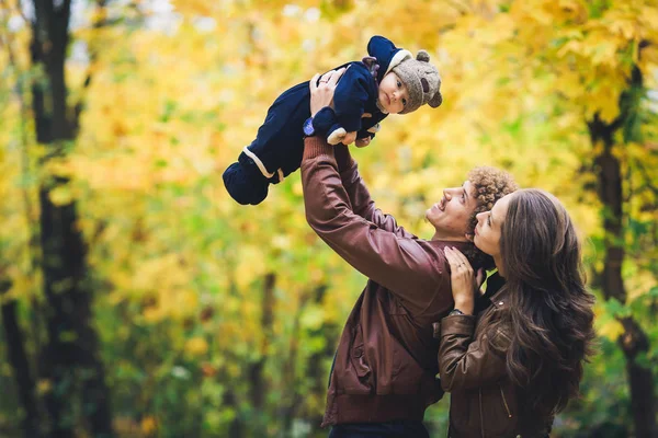 Young happy family in autumn in park. Father joyfully throws his son up. — Stock Photo, Image
