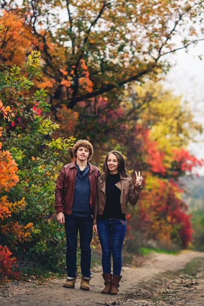 Feliz casal mostra emoções. homem e mulher em jaquetas de couro e jeans contra fundo de árvores de outono . — Fotografia de Stock