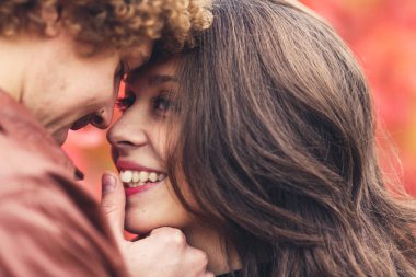 Kıvırcık saçlı bıyıklı adam ve kahverengi saçlı kadın kırmızı ağaçlar çerçevede sonbaharda sarılma.