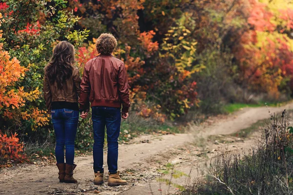 Kręcone włosy facet i dziewczyna blondynem jesienią stałego rozłożonego z plecami na drodze. — Zdjęcie stockowe