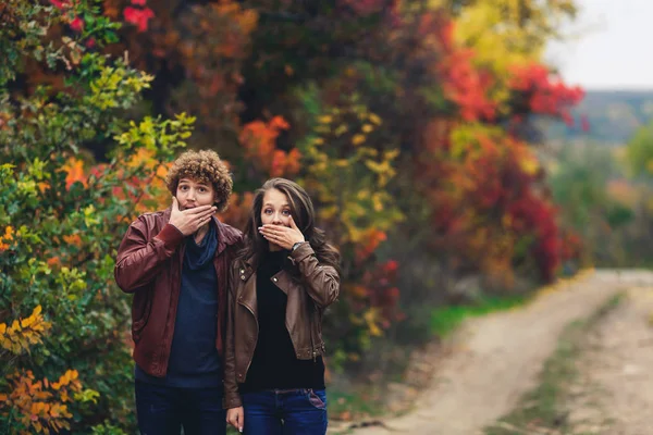 Pareja alegre muestra emociones. hombre y mujer en chaquetas de cuero y jeans muestran sorpresa contra el fondo de los árboles de otoño . — Foto de Stock