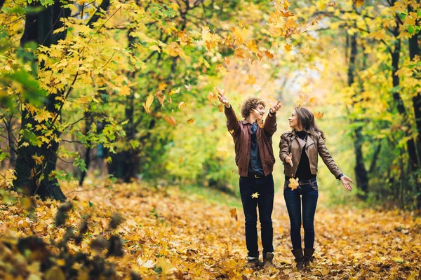 Liebespaar in einem Herbstpark. Mann und Frau werfen munter gelbe Blätter nach oben. — Stockfoto