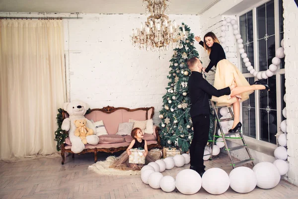 Молода сім'я прикрашає ялинку, рудоволоса дівчина тримає подарунок, сидячи на підлозі . — стокове фото