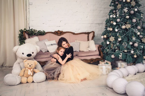 Madre e hija están sentadas en el suelo y abrazándose en Nochebuena . — Foto de Stock