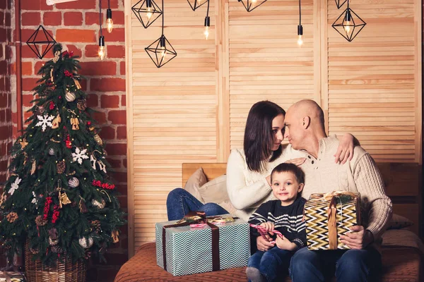 Gelukkige familie zittend op de Bank en holding een riet van het suikergoed en Kerstcadeaus. — Stockfoto