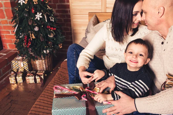 Gelukkige familie zittend op de Bank en holding een riet van het suikergoed en Kerstcadeaus. — Stockfoto