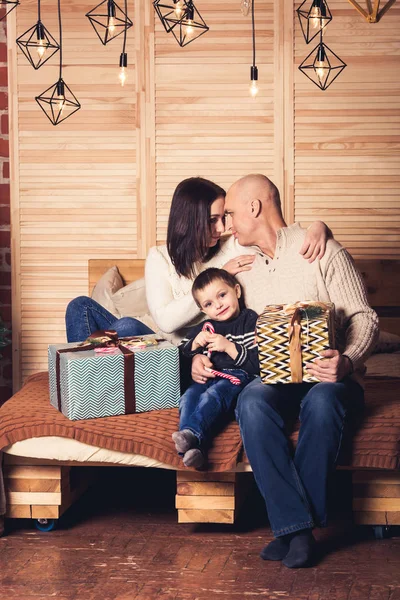 Щаслива сім'я сидить на дивані і тримає цукеркову тростину та різдвяні подарунки . — стокове фото