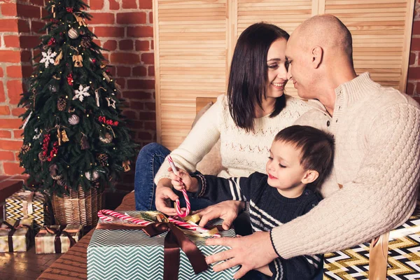 Gelukkige familie zittend op de Bank en holding een riet van het suikergoed en Kerstcadeaus. — Stockfoto