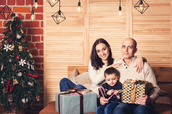 Gelukkige familie zittend op de Bank en holding een riet van het suikergoed en Kerstcadeaus. — Stockfoto