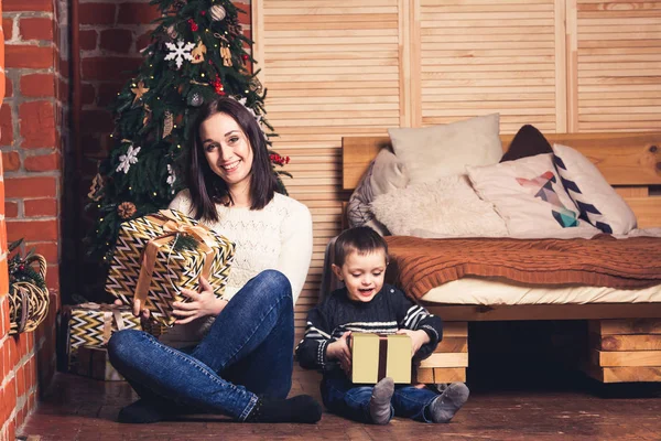 Moeder en zoon zijn zittend op de vloer en houden van Kerst presenteert. — Stockfoto