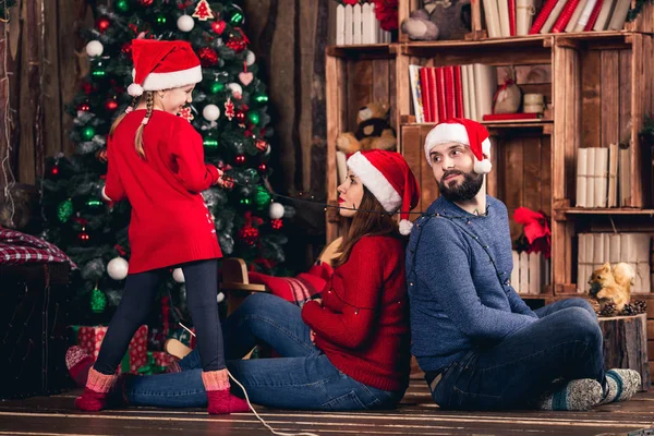 Santa meisje verpakt haar ouders met garland op achtergrond van kerstversiering. — Stockfoto