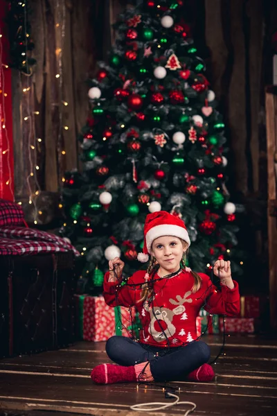 Santa meisje verpakt in garland zittend op de vloer. — Stockfoto