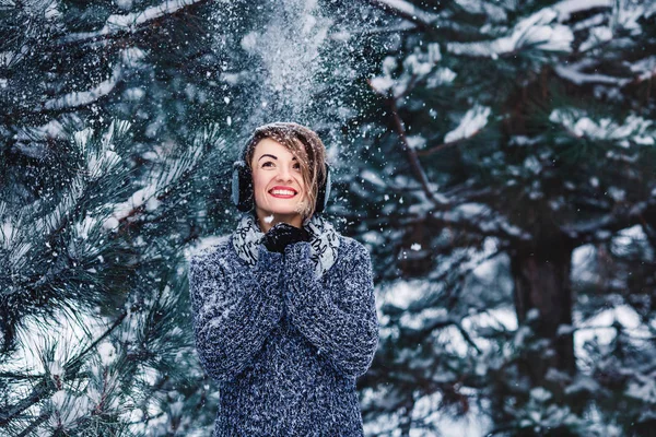 Stylish cheerful girl in a sweater in the winter forest. Snow from tree falls on the girl. — Stock Photo, Image