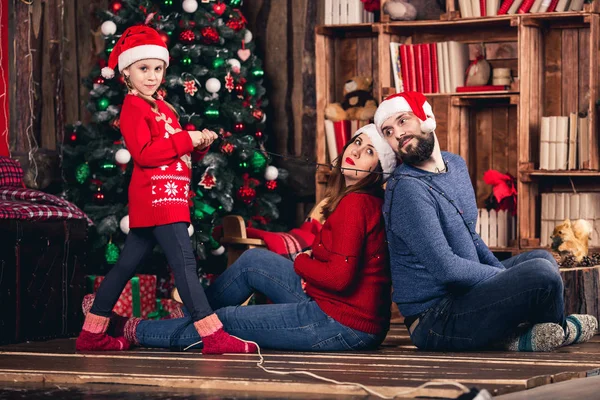 Santa meisje verpakt haar ouders met garland op achtergrond van kerstversiering. — Stockfoto