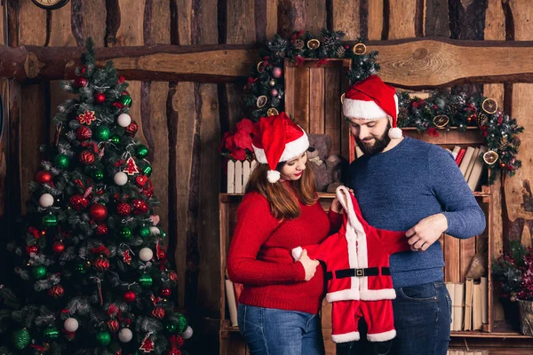 Man en zwangere vrouw houden een kerst kostuum voor de baby. — Stockfoto