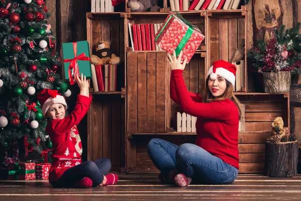 Moeder en dochter zitten op de vloer en houden van Kerst presenteert. — Stockfoto