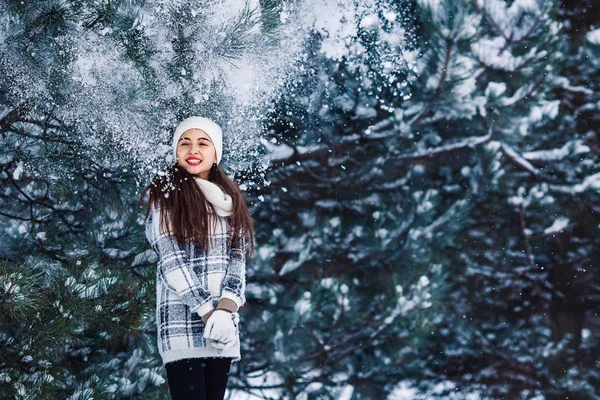 Stylish cheerful girl in a sweater in the winter forest. Snow from tree falls on the girl. — Stock Photo, Image