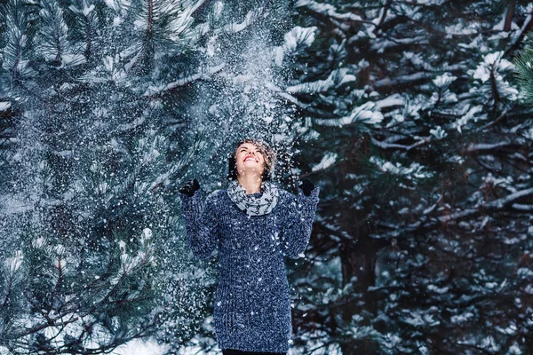 Stylish cheerful girl in a sweater in the winter forest. Snow from tree falls on the girl. — Stock Photo, Image