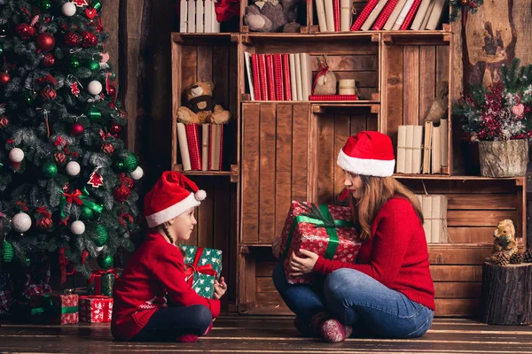 Moeder en dochter zitten op de vloer en houden van Kerst presenteert. — Stockfoto