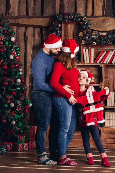 Man, zwangere vrouw en dochter houden een kerst kostuum voor de baby. — Stockfoto