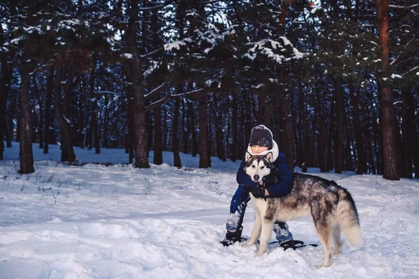 Un adolescente europeo alegre abraza a un perro grande en el invierno en el bosque. El concepto de vacaciones de invierno —  Fotos de Stock