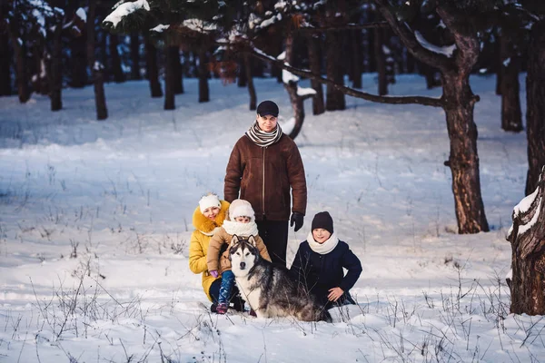 Feliz familia joven europea con gran perro posando contra el bosque de pinos de invierno —  Fotos de Stock