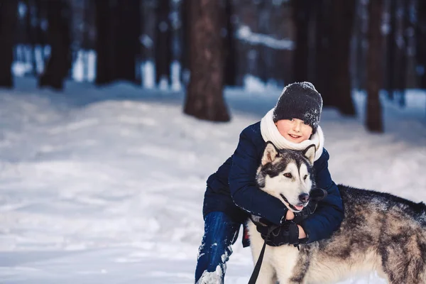 A cheerful European teenager hugs a big dog in the winter in the forest. The concept of winter holidays — Stock Photo, Image
