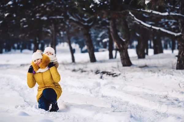 Beautiful young mother and her little daughter are hugging in the winter forest. carrying on piggyback. — Stock Photo, Image